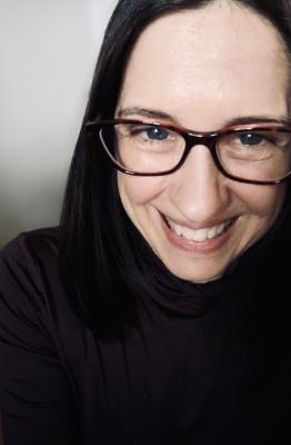 A dark-haired woman wearing glasses and smiling. 